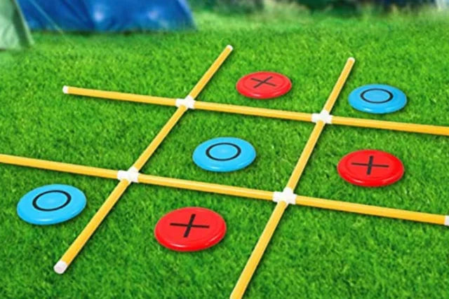 a giant yard tick tack toe set on a green lawn. With red and blue discs.